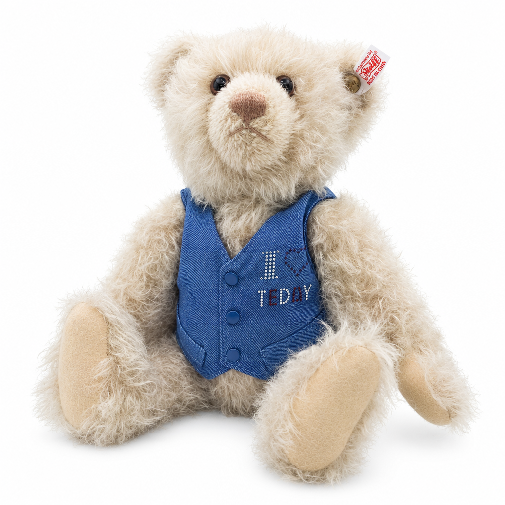 Det här är en kristallnalle från Steiff. Han sitter och pälsen är rufsig, lockig och beige, mjuk och måttligt lång med svag glans, något mörkare kring nospartiet och ögonkanterna. Nospartiet är ljusbrunt och rundat, öronens insida beige och trampdynorna ljust beige. Ögonen är mörkbruna och runda, nosen brun och triangulär. Han bär en avtagbar blå väst med tre blå knappar, text i strass och ett påsytt mörkblått hjärta. Mohair, helt ledad och handgjord.